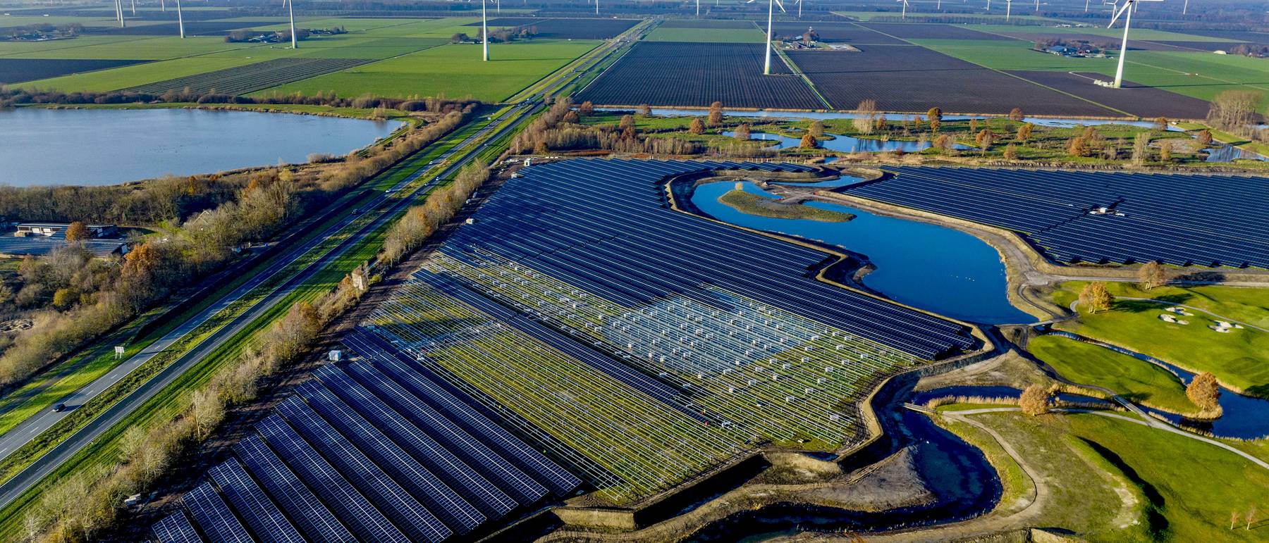 Aerial view of a solar farm with wind turbines on the horizon